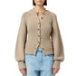 A woman wears the Sculpted Cardigan by Guest in Residence—a beige, long-sleeved cropped cardigan—paired with light blue high-waisted jeans.