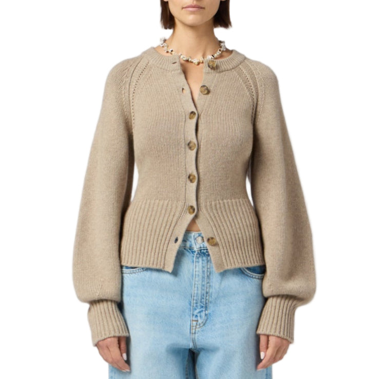 A woman wears the Sculpted Cardigan by Guest in Residence—a beige, long-sleeved cropped cardigan—paired with light blue high-waisted jeans.