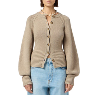 A woman wears the Sculpted Cardigan by Guest in Residence—a beige, long-sleeved cropped cardigan—paired with light blue high-waisted jeans.