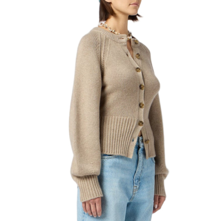 A woman wears the Sculpted Cardigan by Guest in Residence—a beige, long-sleeve style with ribbed cuffs—paired with light blue jeans.