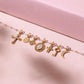 A row of exquisite yellow gold pendants adorned with diamonds, including a cross, oval, circular, diamond-studded cross, pointed cross, and the captivating Moon Pendant by Gigi Clozeau, all elegantly displayed on a soft pink surface.