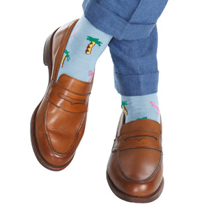 A person wearing brown leather loafers and blue pants with Dapper Classics Sky Blue with Rose Flamingo and Palm Trees Cotton Sock Linked Toe.