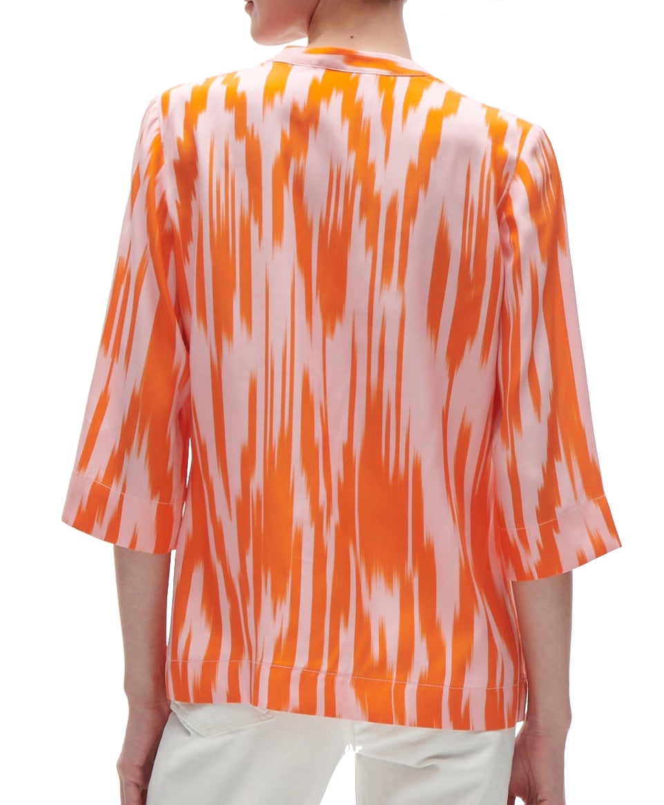 A person from behind wearing a vibrant orange and white Figue Vega Top with a band collar and half sleeves.