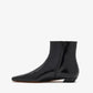 The Proenza Schouler Trap Flat Ankle Boots are black nappa leather with a shiny finish, pointed toe, side zipper, and low heel—displayed in profile against a white background to highlight their sleek, modern silhouette.