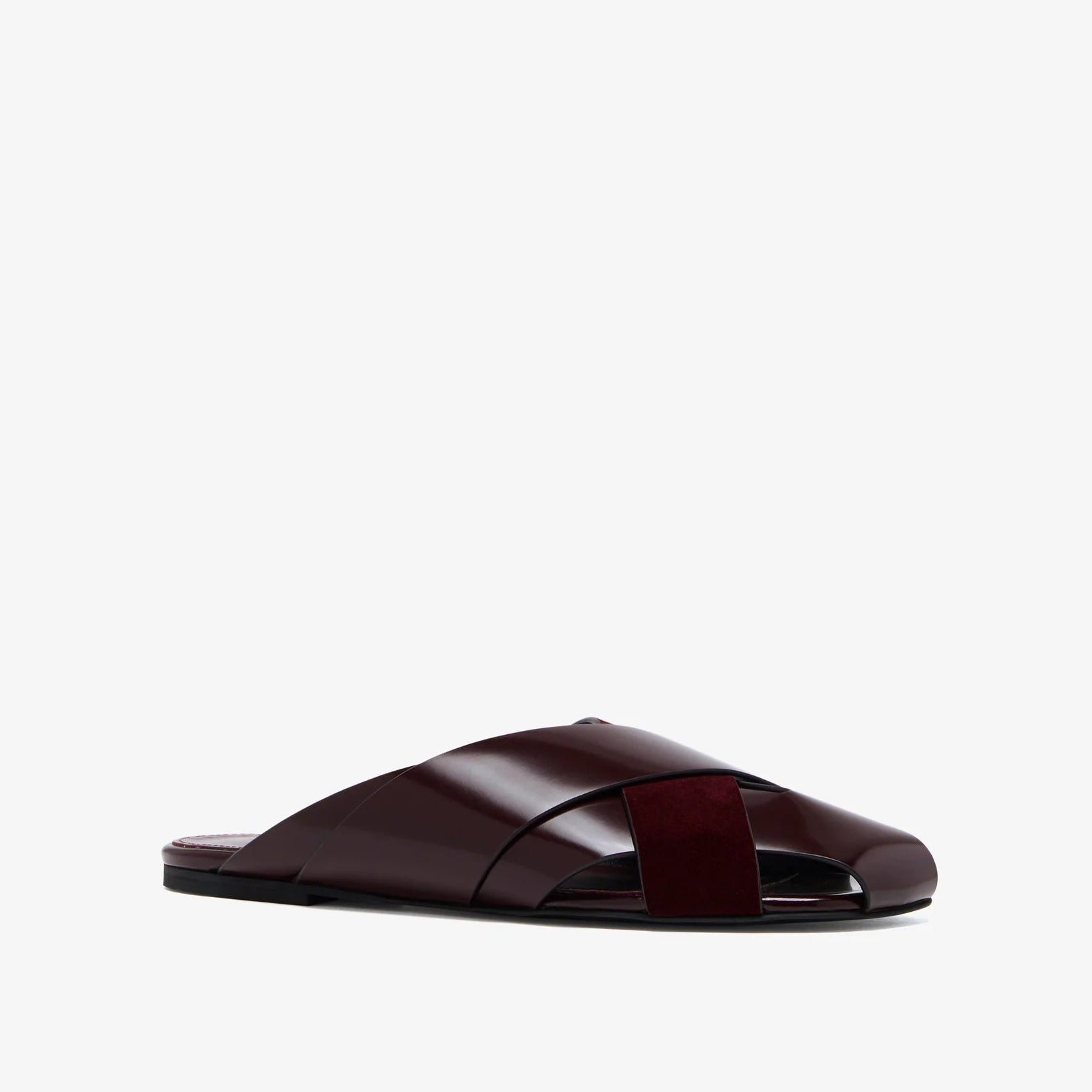 The Proenza Schouler Slant Cross Slides is a single burgundy sandal with wide crisscross brushed calf suede straps and a flat sole, displayed against a plain white background.