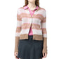 A person wearing a pink collared shirt, Guest in Residence Shadow Plaid Cardigan in light brown and white stripes, and a dark pleated skirt stands against a white background.