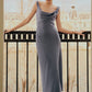 A woman stands on a balcony overlooking a river and historic buildings, wearing the Lela Rose Linen Twist Detail Dress—a sleeveless, light blue, anti-wrinkle linen piece with an A-line skirt.