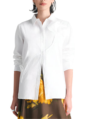 A woman stands facing forward wearing the Lela Rose Draped Rose Button Down Shirt, a long-sleeved cotton poplin shirt, paired with a brown skirt featuring a yellow floral pattern.