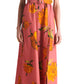 A woman models the Lela Rose Asymmetrical Cuff Dress—pink, off-shoulder with yellow floral print and cinched waist—paired with black open-toe heels, standing against a plain white background.