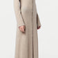 A person stands in profile wearing the Guest in Residence Showtime Cashmere Shirt Dress, a lightweight beige button-down with flared sleeves, paired with white sneakers against a plain background.