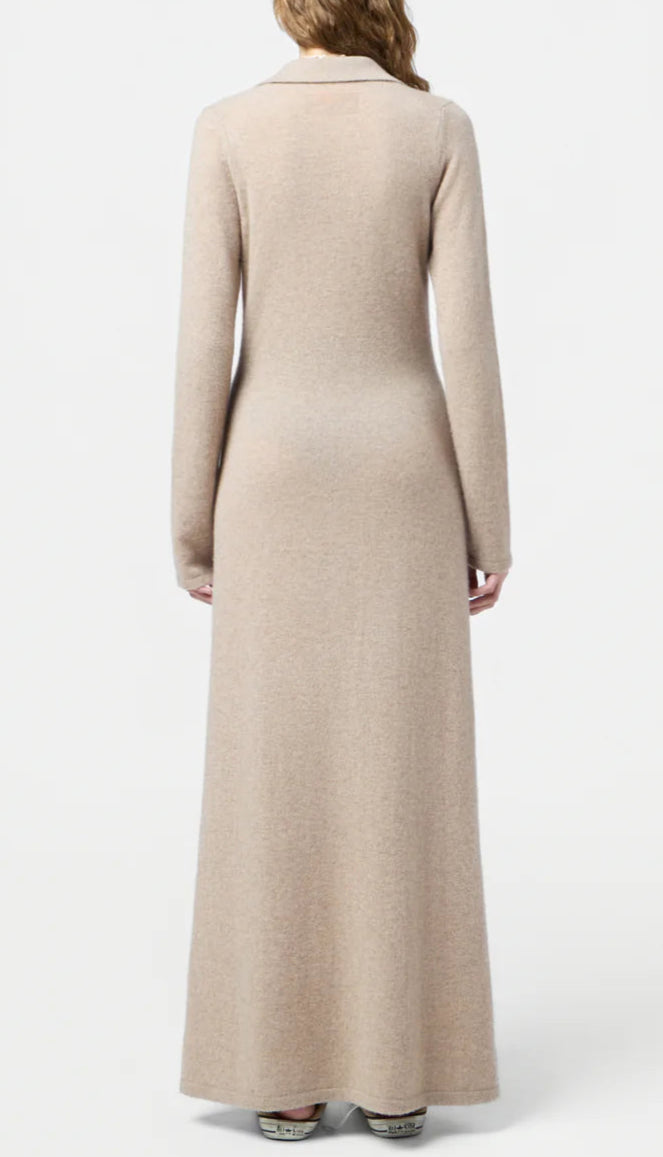A person stands facing away on a plain white background, wearing the Showtime Cashmere Shirt Dress by Guest in Residence—a long-sleeved, full-length, lightweight beige piece.