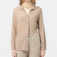 A person wearing the beige Showtime Cashmere Shirt by Guest in Residence with matching pants and a beaded necklace stands against a plain light background.