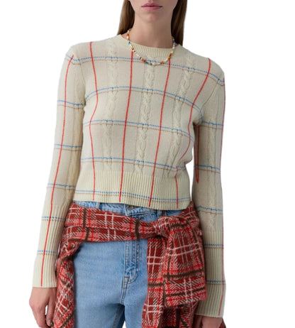 A woman wears the Guest in Residence Shrunken Check Crew, a cream jacquard women’s sweater with red and blue plaid pattern, paired with blue jeans and a red plaid shirt tied at her waist, against a white background.