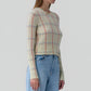 A woman wears the Shrunken Check Crew sweater by Guest in Residence, featuring cream with red and blue check jacquard details, paired with light blue high-waisted jeans.