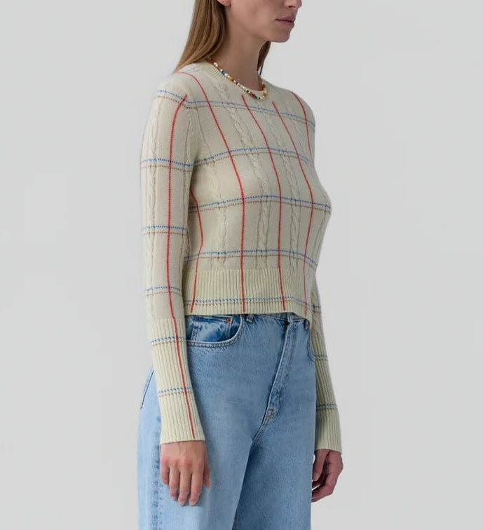 A woman wears the Shrunken Check Crew sweater by Guest in Residence, featuring cream with red and blue check jacquard details, paired with light blue high-waisted jeans.