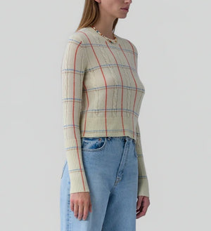 A woman wears the Shrunken Check Crew sweater by Guest in Residence, featuring cream with red and blue check jacquard details, paired with light blue high-waisted jeans.