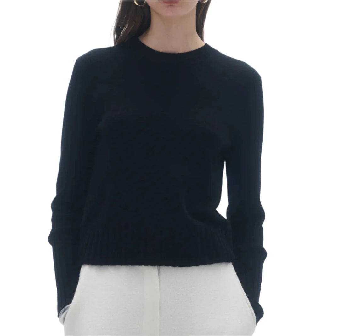 A person is seen wearing the Guest in Residence Shrunken Crew Cashmere Sweater and white pants, with hands in pockets, set against a plain white background.