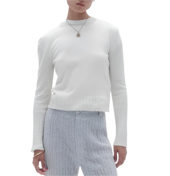 A person wearing the Guest in Residence Shrunken Crew Cashmere Sweater in white, paired with light gray pants and accessorized with a necklace. The lightweight knit of the sweater adds an elegant touch to the ensemble.