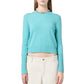 Woman wearing the Shrunken Crew Cashmere Sweater by Guest in Residence in turquoise, paired with cream pants, stands against a white background. The sweater features a slim fit and ribbed trim.