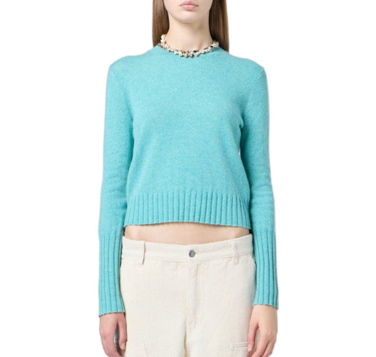 Woman wearing the Shrunken Crew Cashmere Sweater by Guest in Residence in turquoise, paired with cream pants, stands against a white background. The sweater features a slim fit and ribbed trim.