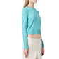 A woman stands in profile wearing the Guest in Residence Shrunken Crew Cashmere Sweater with cream-colored pants, set against a white background.