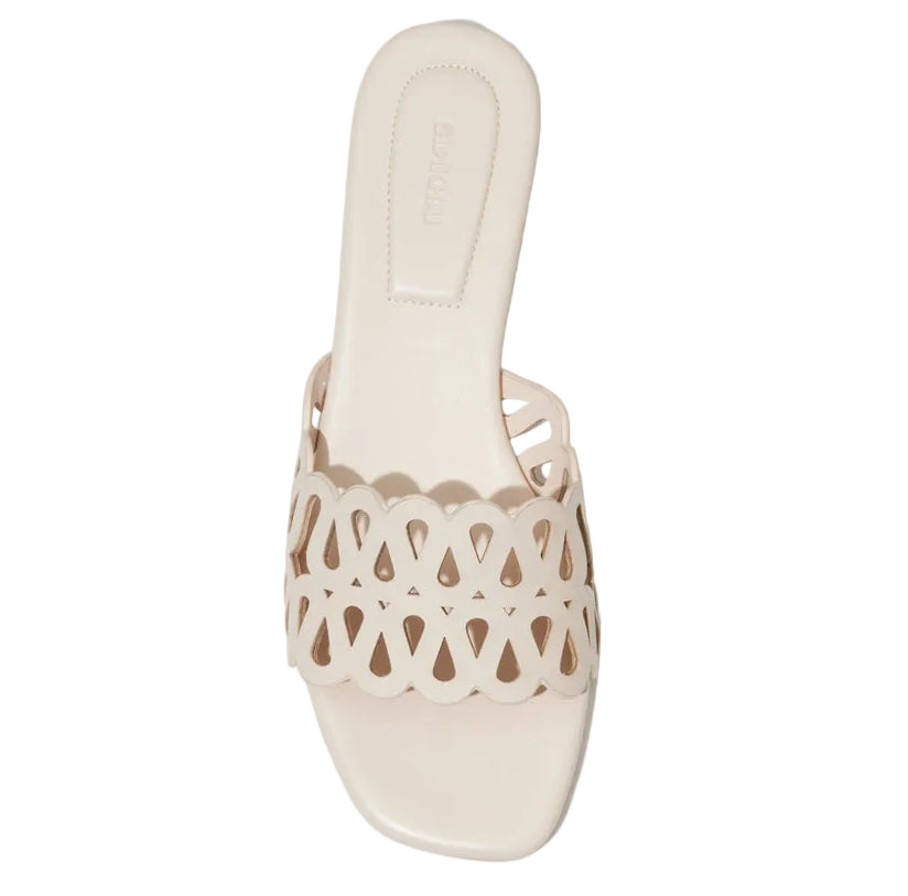 The McCall Laser Cut Flat Slide by Simkhai is an off-white leather slip-on sandal with a scalloped, cut-out strap and square toe.