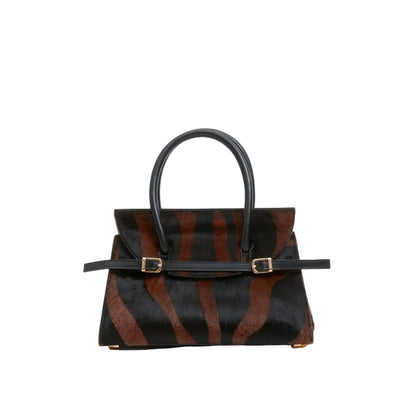 The Simkhai River Small Top Handle Bag showcases a bold black and brown zebra-print calf hair design with a striking stripe pattern. Featuring top handles, gold buckles, and a structured rectangular silhouette, this elegant bag comes with an optional crossbody strap for added versatility, all shown against a crisp white background.