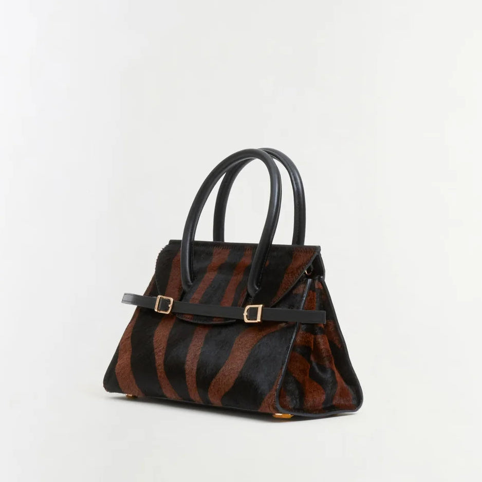 The Simkhai River Small Top Handle Bag is a structured accessory featuring black leather handles, a brown and black striped pattern, gold hardware, and a detachable crossbody strap, all showcased against a plain white background.