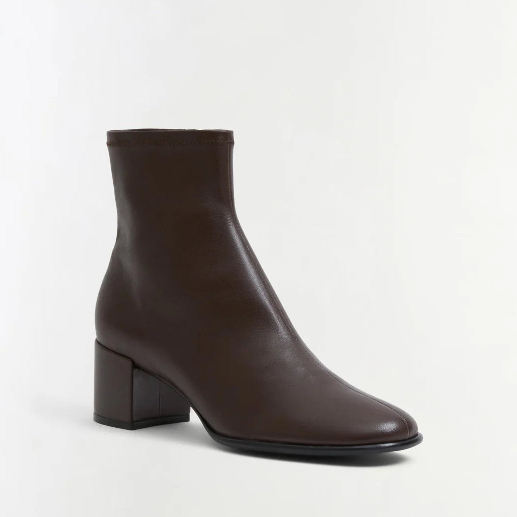 The Bianca Stretch Leather Ankle Boot by Simkhai is a dark brown ankle boot featuring a rounded toe and a low, chunky block heel, shown against a plain white background.