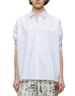 A person is shown from the front wearing the Callas Milano Sirene Top, a loose-fitting white cotton poplin shirt with long sleeves, paired with printed cream pants featuring a subtle seashell design.