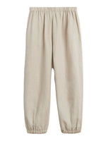 The Delos Pants by Suzie Kondi feature a ruched waist and elastic leg hem in beige linen, creating a versatile silhouette. Shown against a plain white background.