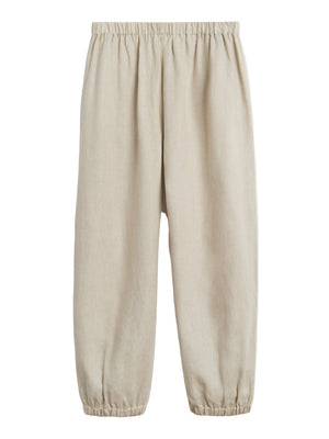 The Delos Pants by Suzie Kondi feature a ruched waist and elastic leg hem in beige linen, creating a versatile silhouette. Shown against a plain white background.