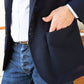 A person wearing a Sid Mashburn Ghost Blazer with unlacquered brass buttons, a light-colored shirt, and jeans with one hand placed in the jacket's pocket.