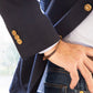 A person wearing a navy Sid Mashburn Ghost Blazer with unlacquered brass buttons and jeans, complemented by a brown bracelet on their wrist. Their hand is resting on their hip.