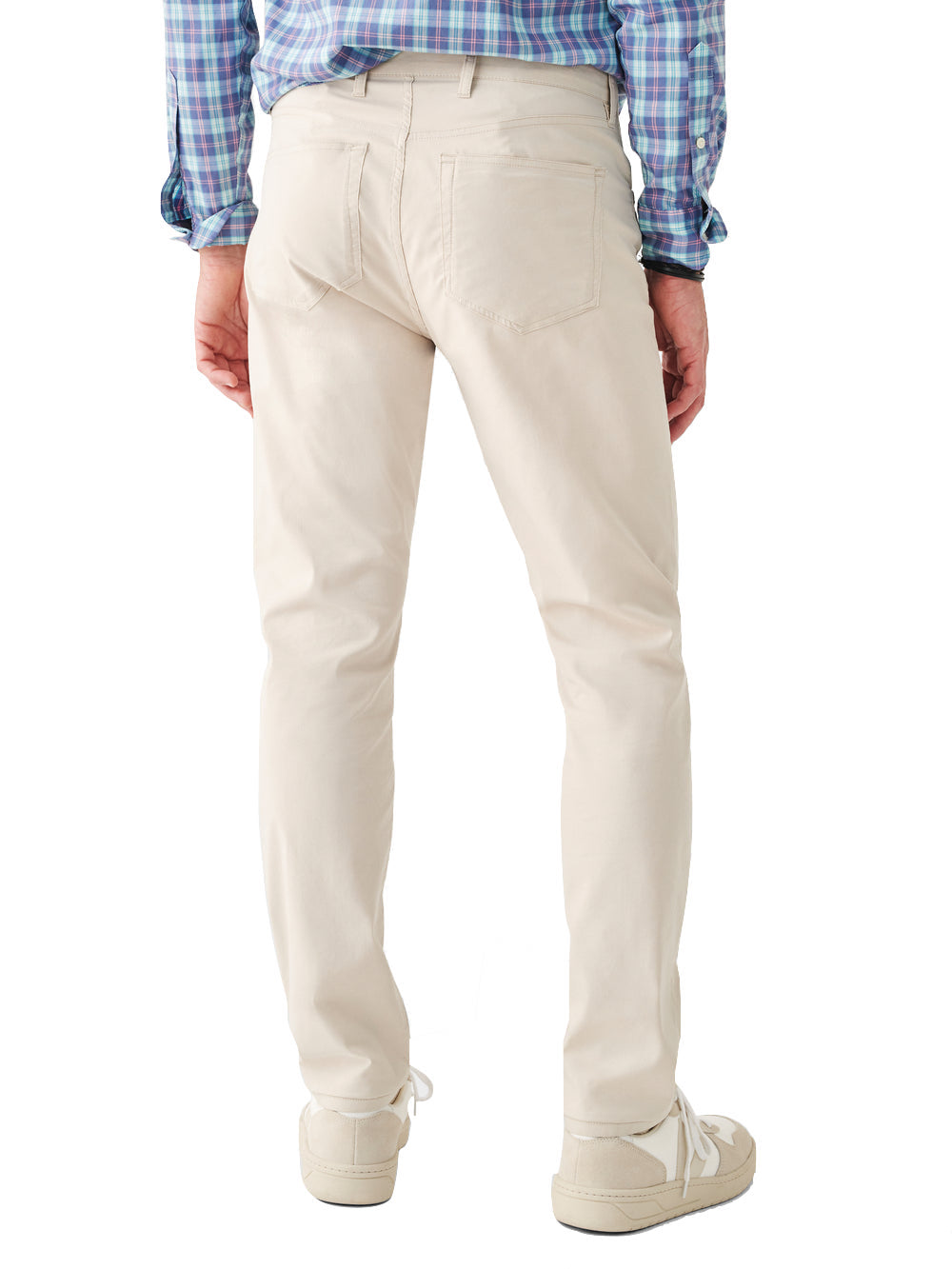 A person standing with their back toward the camera, wearing Faherty Movement Five Pocket Pant beige pants with 4-way stretch, a blue and white checkered shirt featuring COOLMAX® CORE Technology, and beige shoes.