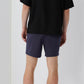 A person faces away from the camera, wearing a black T-shirt and Onia Land to Water Short 6" in navy blue with four-way stretch, against a plain background.