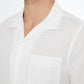A close-up of a man wearing the Onia Air Linen Convertible Vacation Shirt, shown from shoulders to chin. The shirt features a camp collar, white linen-tencel blend, chest pocket, and open neckline.