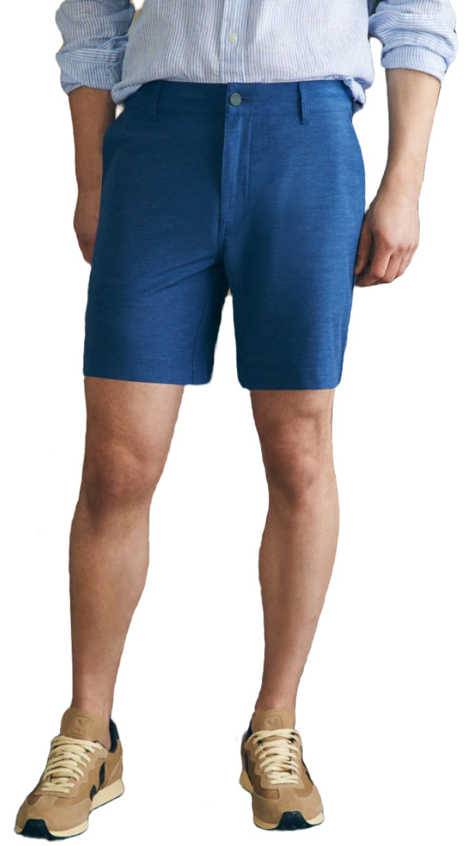 Person in a striped shirt, Faherty's eco-friendly Belt Loop All Day Shorts, 7", and beige sneakers, against a plain backdrop.