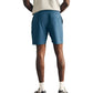 A person stands facing away, wearing a gray t-shirt and Faherty Shorelite Swim Trunks—blue athletic shorts crafted from quick-drying fabric—along with white socks and black sneakers, hands resting on their hips against a plain white background.
