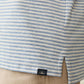 Close-up of Faherty's Short-Sleeve Movement™ Polo Shirt, featuring blue and white stripes with a small black tag above a side slit, paired with tan pants. Designed for effortless ease of movement, it combines performance qualities for comfort and style in every stride.