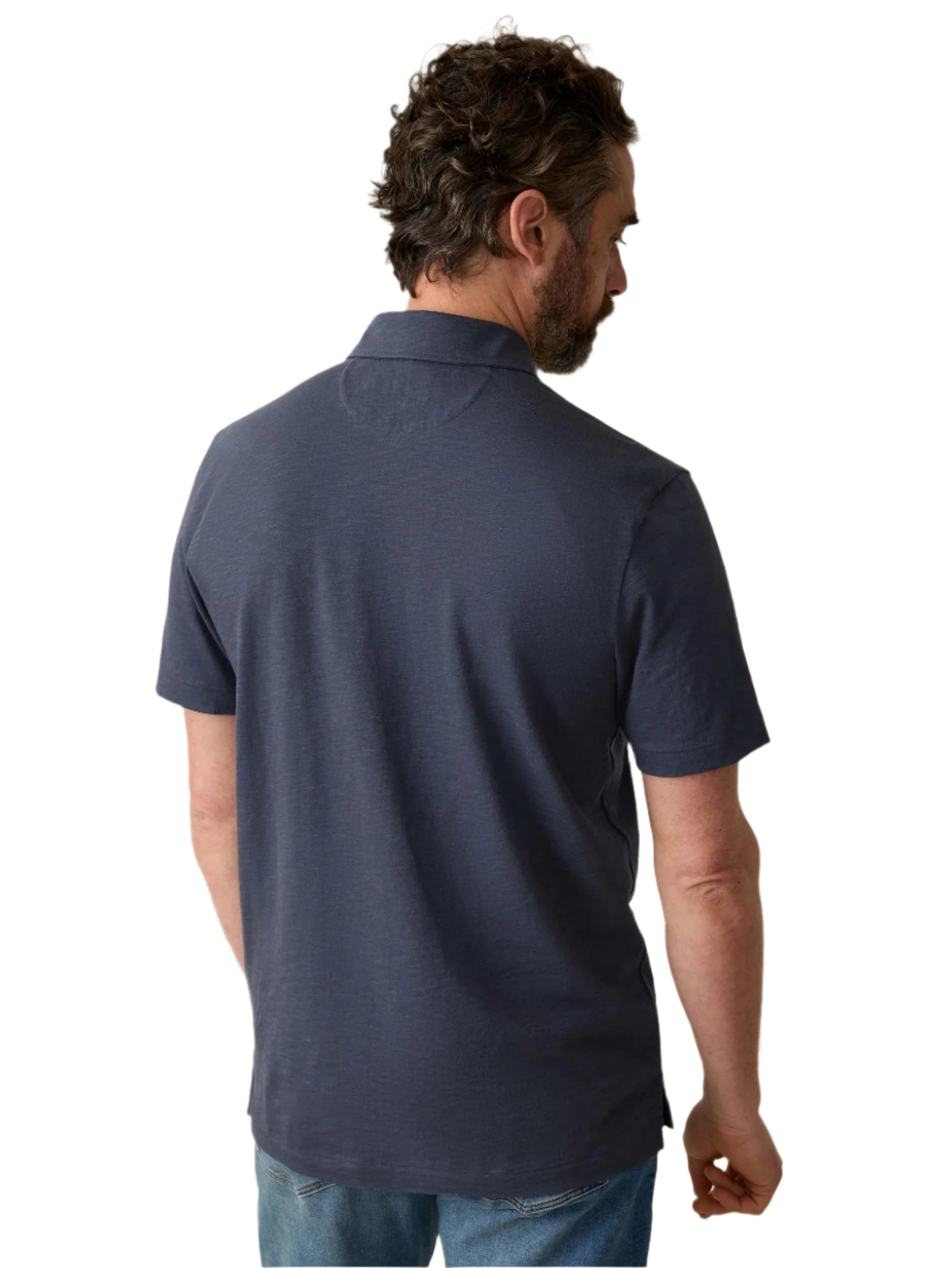 A man with short curly hair, wearing a dark Faherty Sunwashed T-Shirt Polo made from regenerative organic cotton and jeans, is seen from the back against a white background.