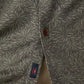 A close-up of Faherty's Short-Sleeve Hermosa Shirt in soft TENCEL™ shows a green leaf-patterned fabric with a brown button and a small tag featuring a colorful bird design near the hem.