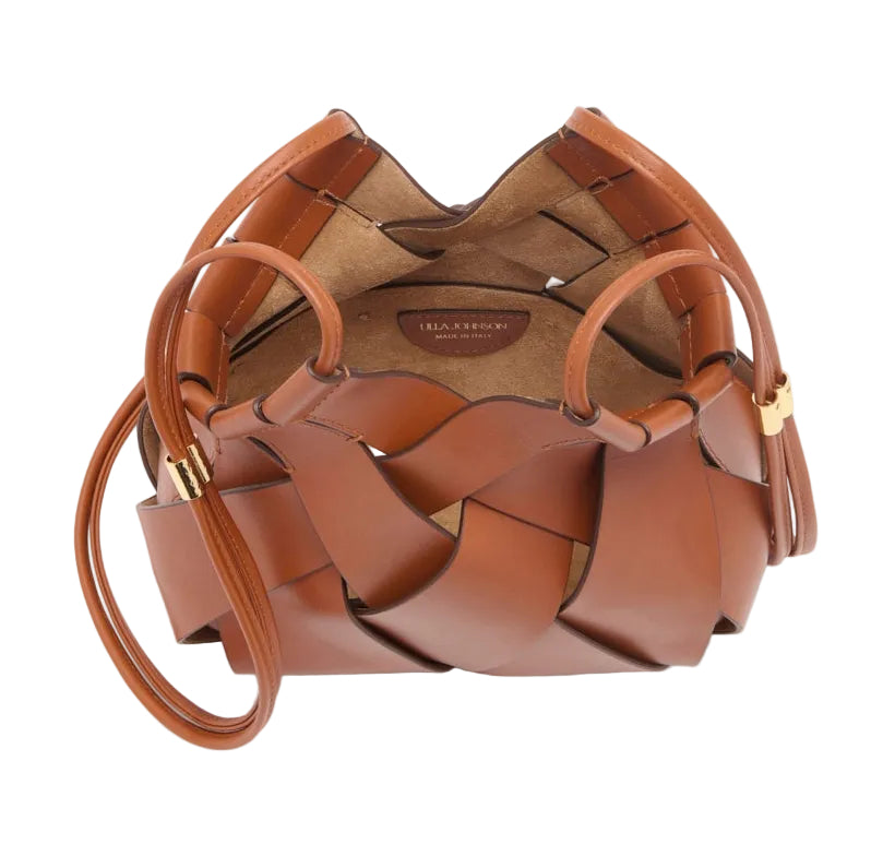 The Charlotte Crossbody by Ulla Johnson is a brown woven calfskin leather handbag with an open top, round base, and thin side strap. Artisanal craftsmanship shines in every detail; interior label reads “ILLA STEWART.”.