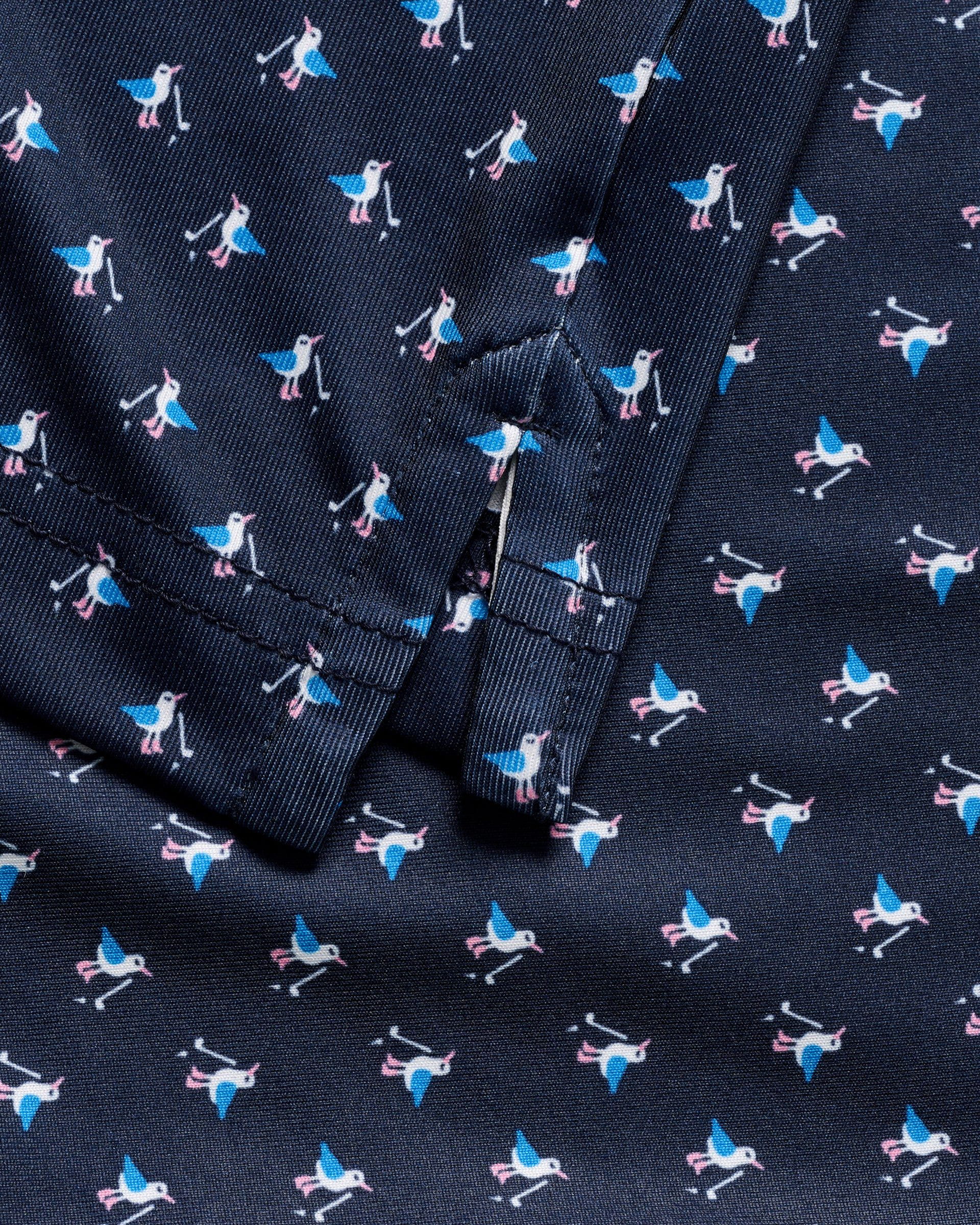 Close-up of the Johnnie-O Boys' Performance Jersey Jr. Polo in For The Birdies Print shows soft navy fabric with white and blue birds with pink beaks and feet, plus seam and folded edge details that highlight this unique polo material.