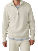 Against a white background, a person in Faherty's High Standard Fleece Quarter Zip and matching pants exudes timeless style. Their tattooed hands add a personal touch to the ensemble.