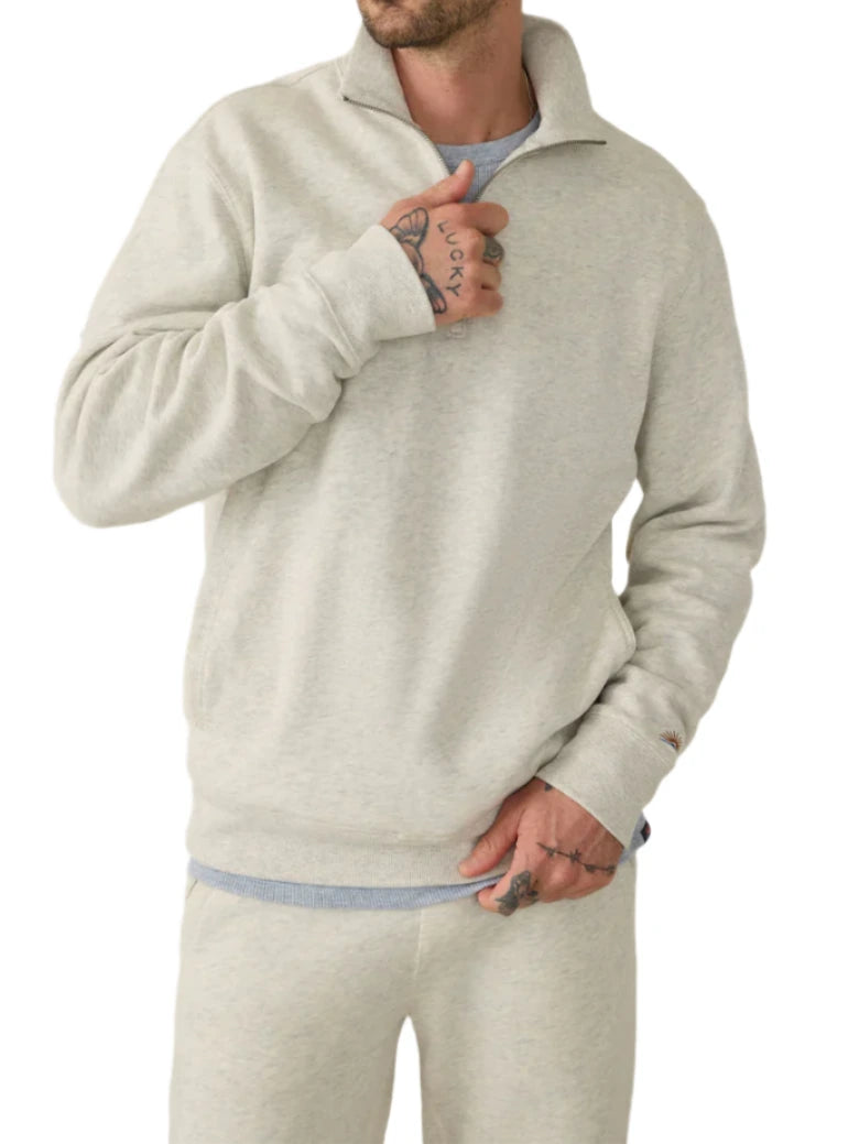 A person exudes timeless style in a Faherty High Standard Fleece Quarter Zip in light grey, paired with matching sweatpants, tattoos adorning their hands.