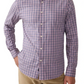 A man is wearing the Faherty Movement Sport Shirt, a long-sleeve button-up made from wrinkle-resistant Supima cotton, featuring a pink and blue plaid pattern. He pairs it with beige pants.