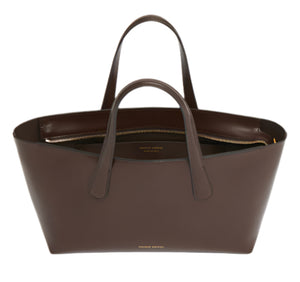 The Mansur Gavriel Mini Everyday is a compact brown tote crafted from Italian spazzolato leather, featuring short handles, an internal zip compartment for essentials, and an adjustable crossbody strap for versatile carrying.