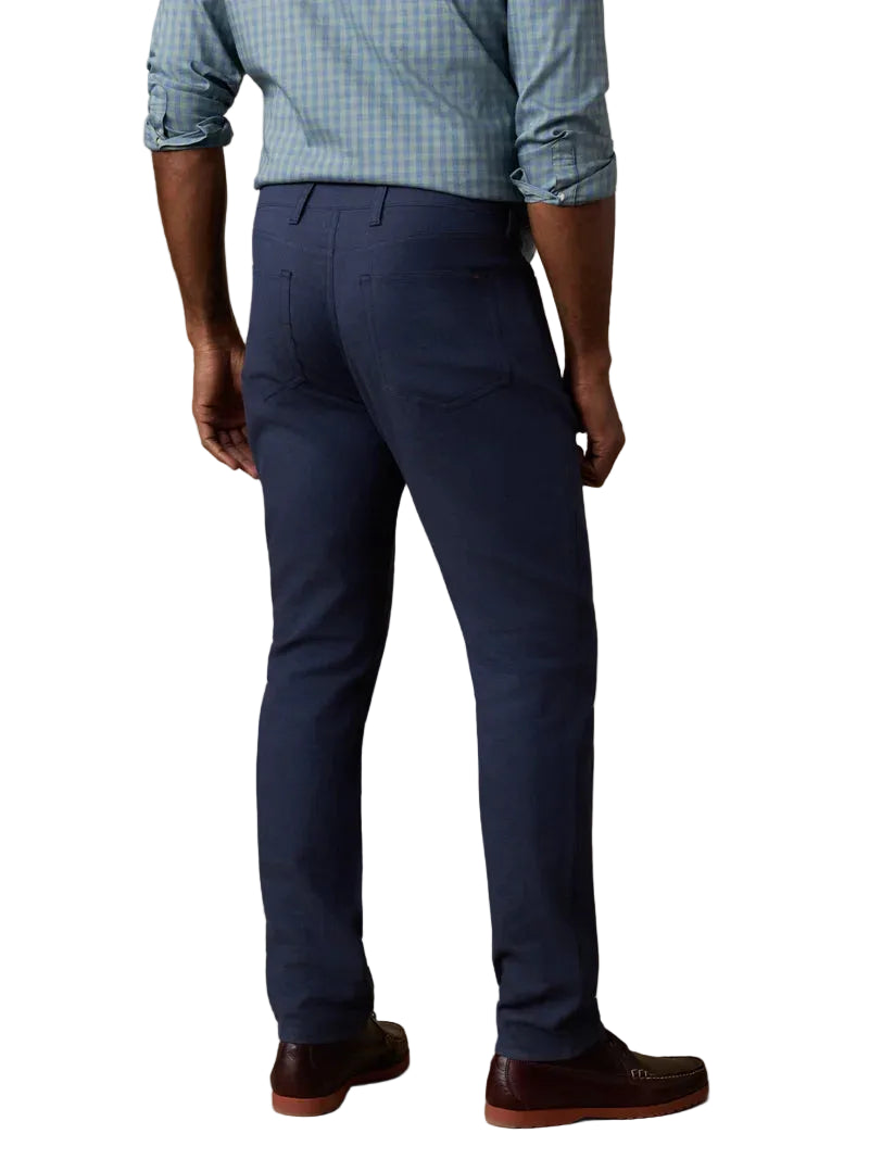 Man wearing a blue checked long-sleeve shirt, Faherty Movement Linen 5-Pocket Pant in navy blue, and brown shoes, shown from the back.