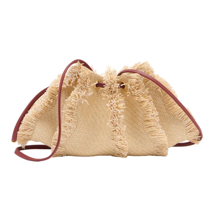 The Adria Small Crossbody by Ulla Johnson is a woven beige straw raffia handbag with frayed edges, brown leather straps, and a removable shoulder strap, shown on a white background.